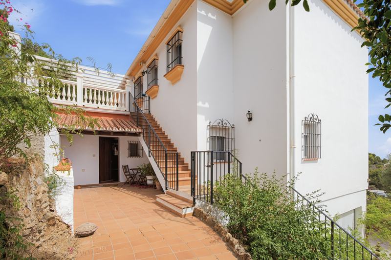 Fachada encalada de la villa con escalera exterior y terraza al sol